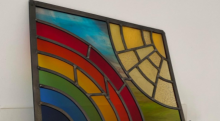 Image of multicoloured stained glass artwork in the shape of a rainbow and sun